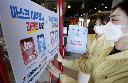 12일 오전 광주 북구의 한 커피숍에서 광주 북구보건소 감염병관리팀 직원들이 마스크 착용 의무화 시행으로 13일부터 미착용 시 과태료를 부과한다는 안내문을 붙이고 있다.  광주=연합뉴스